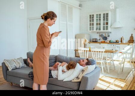 Woman photographing man sleeping with daughter on sofa at home Stock Photo
