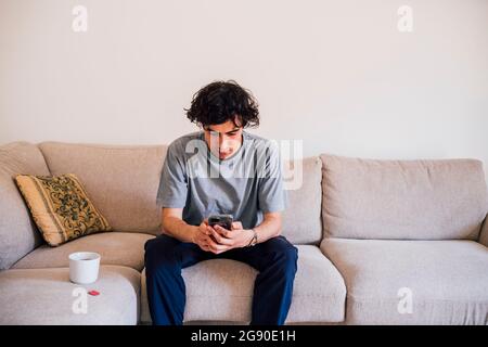 Man using mobile phone while sitting by coffee cup on sofa Stock Photo