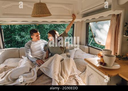 Smiling young man looking at girlfriend stretching while waking up in motor home Stock Photo