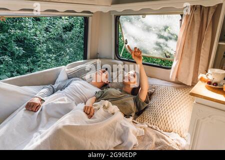 Young woman pointing up while lying by boyfriend on bed in motor home Stock Photo