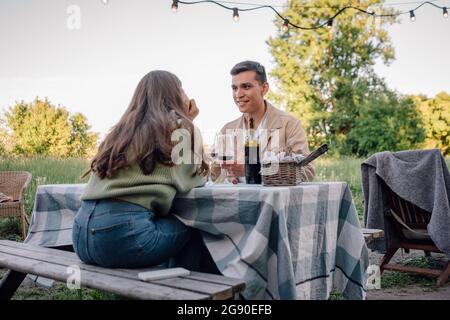 Smiling young man looking girlfriend sitting on bench Stock Photo