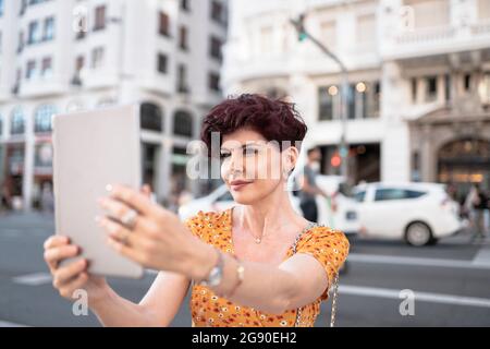 Mature woman taking selfie through digital tablet in city Stock Photo