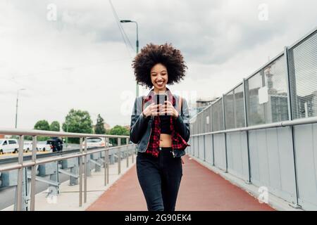 Happy woman using mobile phone while walking on footpath Stock Photo