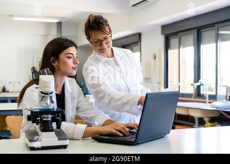 Mature female scientist and young colleague discussing over laptop at laboratory Stock Photo