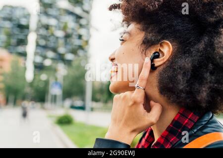 Cheerful young woman touching wireless in-ear headphones Stock Photo