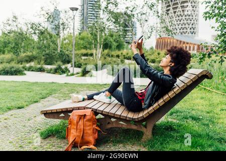 Woman taking selfie through smart phone while sitting on wooden chair at park Stock Photo