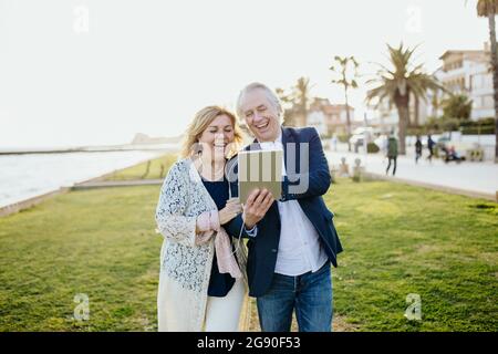 Happy mature couple sharing digital tablet while watching video during vacation Stock Photo