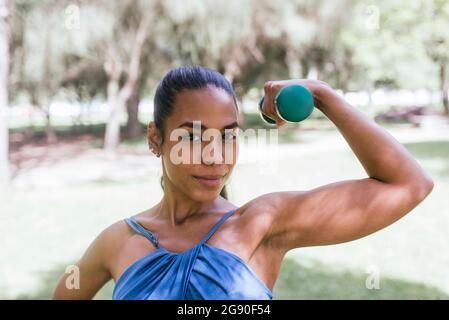 Young female athlete with dumbbell exercising at park Stock Photo