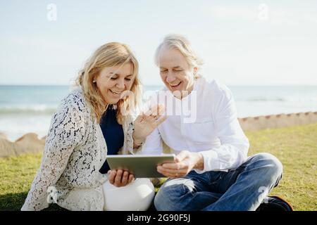 Happy mature woman waving hand on video call while man holding digital tablet during vacation Stock Photo