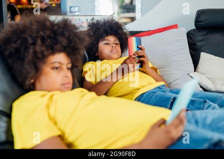 Twin brothers using wireless technologies on sofa at home Stock Photo