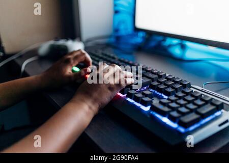 Boy playing game on computer through illuminated keyboard at home Stock Photo
