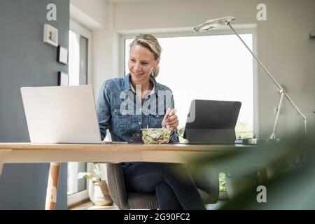 Female freelance worker using laptop while sitting at home office Stock Photo