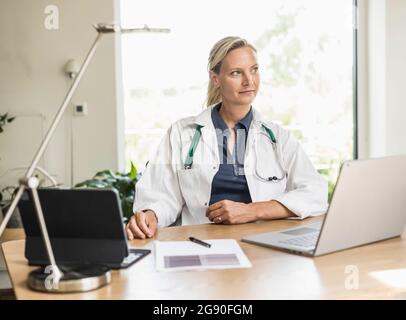 Thoughtful female doctor looking away while sitting at office Stock Photo