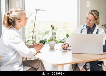 Doctor writing on paper while sitting with patient at office Stock Photo