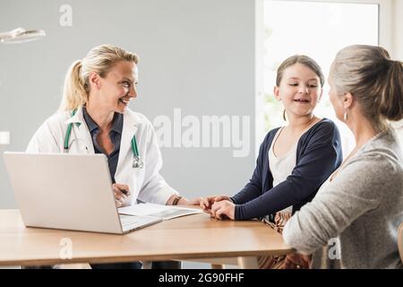 Daughter talking with mother while sitting by doctor at office Stock Photo