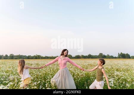 Mother holding hands of children while walking amidst flowers in field Stock Photo