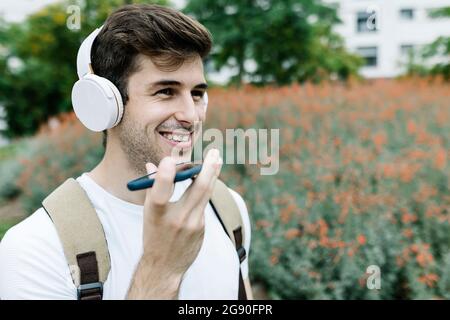 Smiling young man sending voicemail through mobile phone by meadow Stock Photo