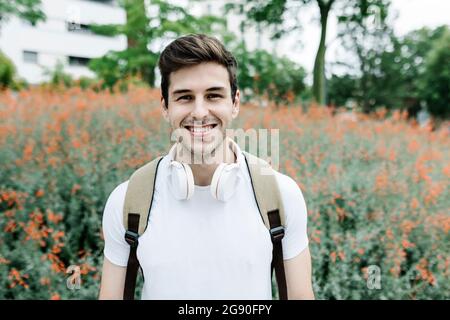 Smiling young man carrying backpack while standing in front of meadow Stock Photo