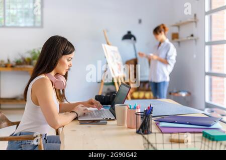Female photographer using laptop while artist painting in studio Stock Photo