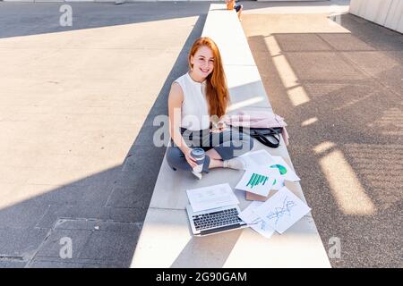 Young female professional with mobile phone having coffee on bench Stock Photo