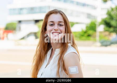 Redhead female professional with bandage on arm smiling during COVID-19 Stock Photo