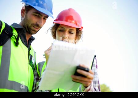 Male and female engineers discussing while holding document Stock Photo