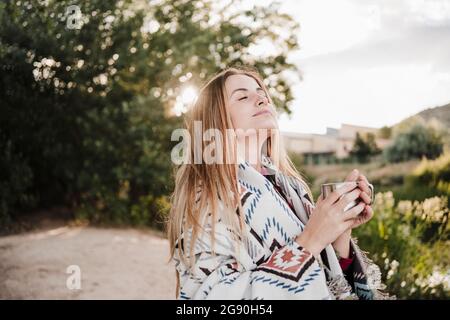 Beautiful blond woman with eyes closed wrapped in blanket coffee mug Stock Photo