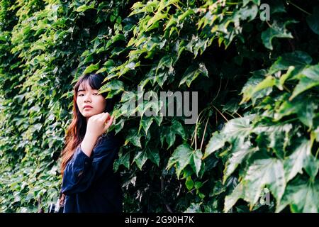 Young female photographer with camera standing in front of plants Stock Photo