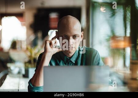 Thoughtful bald male cafe owner using laptop Stock Photo