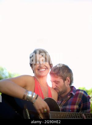 Man kissing shoulder of girlfriend playing guitar Stock Photo