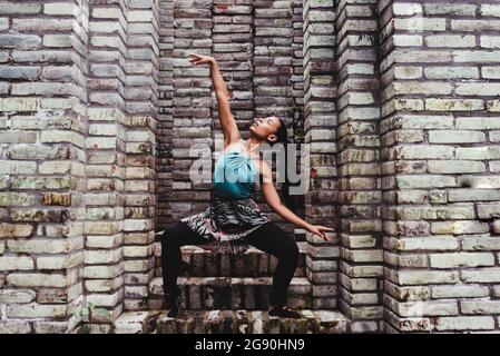 Young female dancer practicing dance amidst stone walls Stock Photo