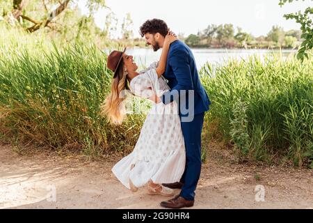 Happy man holding cheerful woman wearing hat at park Stock Photo