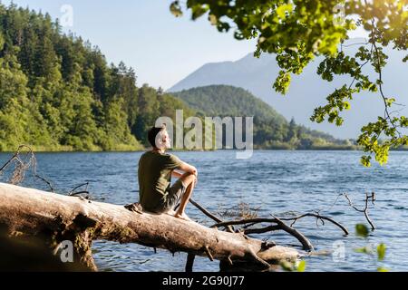 Man looking at view while siting on fallen tree at lake Stock Photo