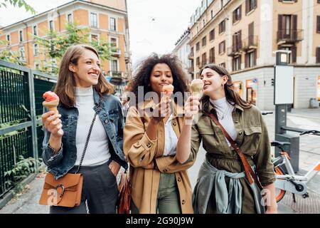 Smiling friends having ice cream while walking in city Stock Photo