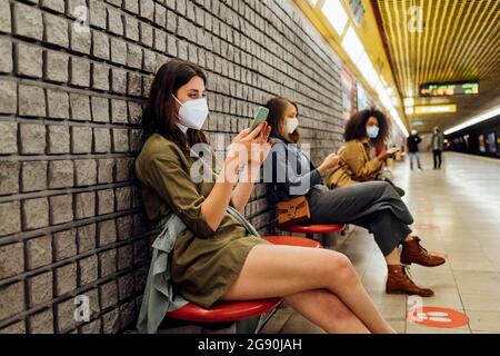Woman wearing face mask using mobile phone while sitting at social distance in subway Stock Photo