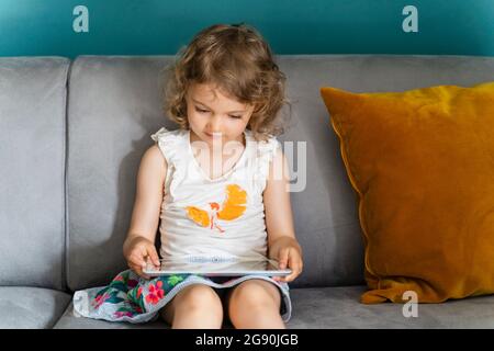 Girl using digital tablet while sitting on sofa at home Stock Photo