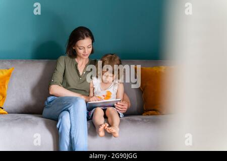 Mother helping daughter using digital tablet while studying at home Stock Photo