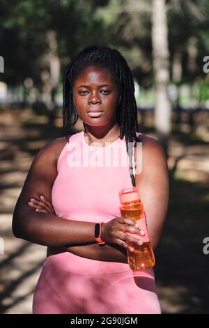 Confident young curvy woman with arms crossed holding water bottle Stock Photo