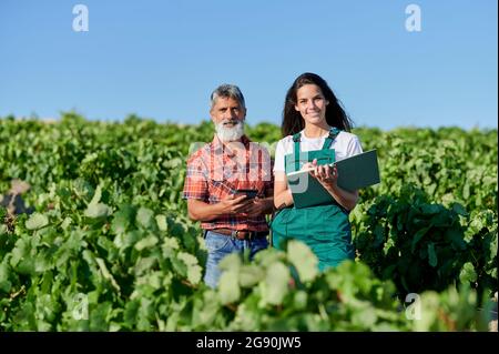 Smiling female farmer with book standing by man in vineyard Stock Photo