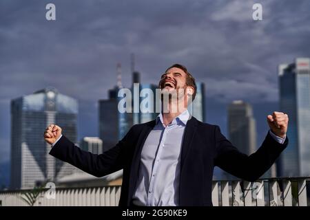 Happy male professional with eyes closed making fists while celebrating success on rooftop Stock Photo