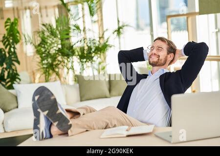 Smiling relaxed male professional sitting with feet up on table in home office Stock Photo