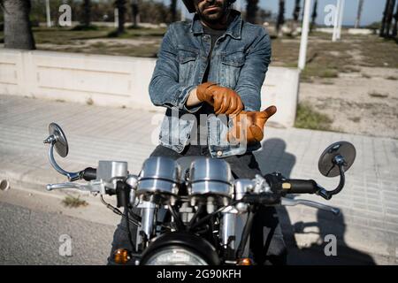 Young man wearing gloves while sitting on motorcycle Stock Photo