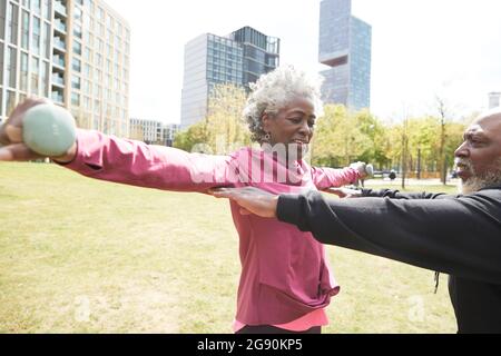Man assisting senior woman in exercising at park Stock Photo