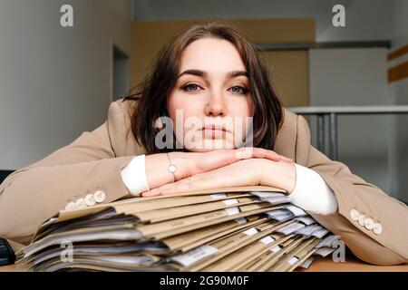 Young businesswoman leaning on stack of file at desk in office Stock Photo