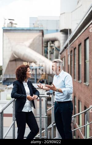 Male and female professionals having discussion while standing by railing Stock Photo
