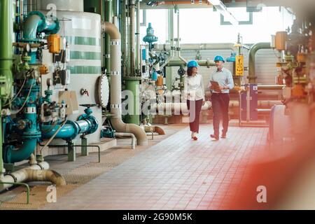 Male and female engineers discussing while walking in workshop Stock Photo