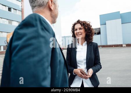 Smiling businesswoman talking with colleague while standing on footpath Stock Photo