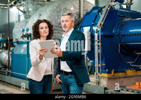 Male and female expert using digital tablet while standing at power station Stock Photo