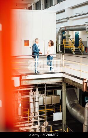 Male and female colleagues having discussion while standing in industry Stock Photo