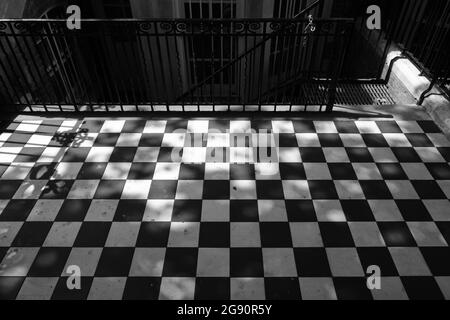 Black and white image of checkered pattern floor. Wrought iron fence and staircase in the background. Stock Photo